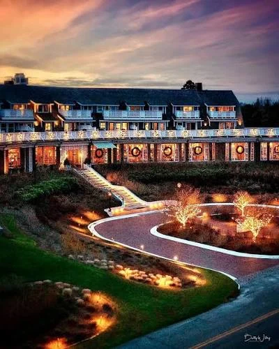 An illuminated Cape Cod building and landscaped grounds at dusk